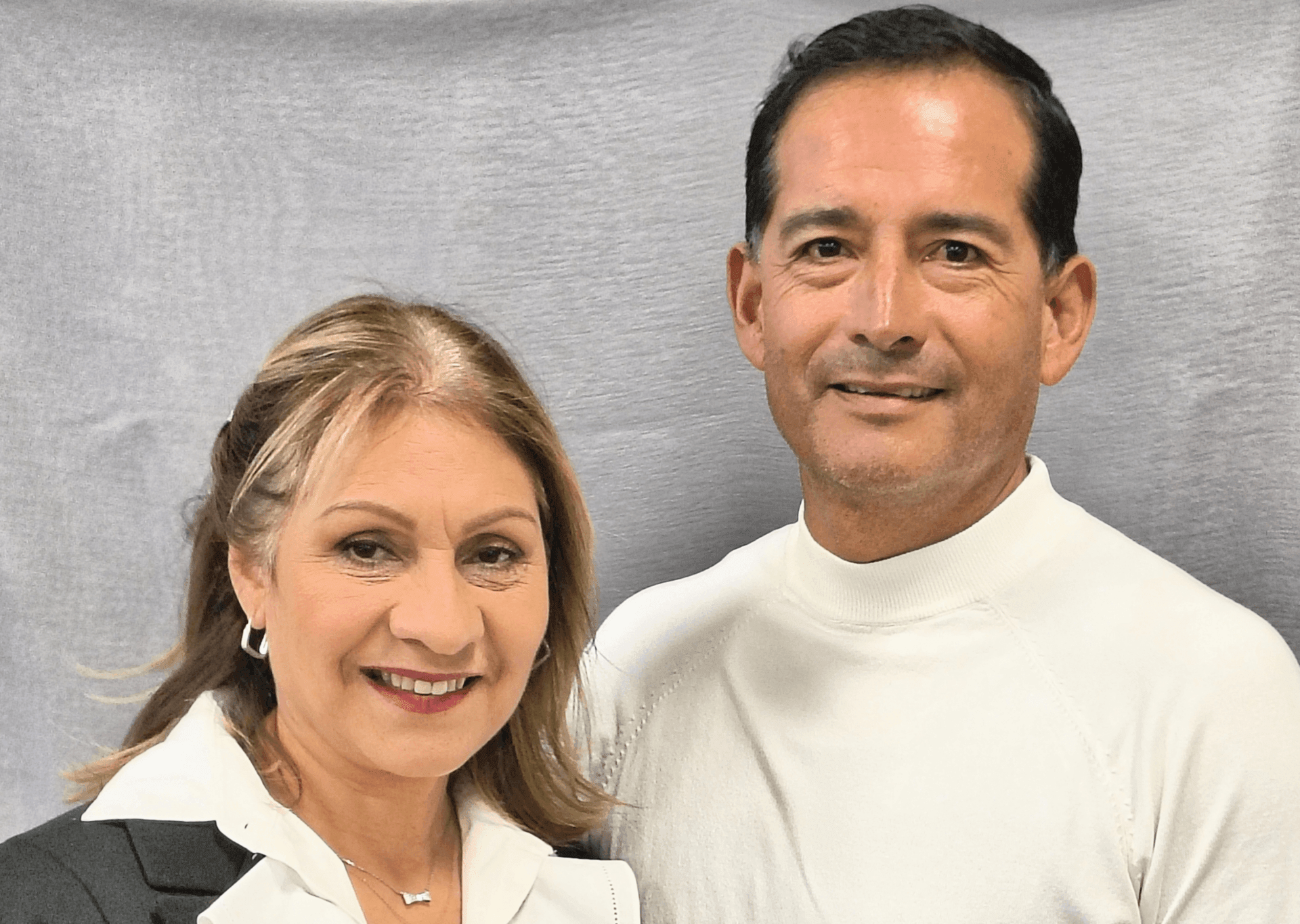 Smiling man and woman standing side by side with a gray backdrop.