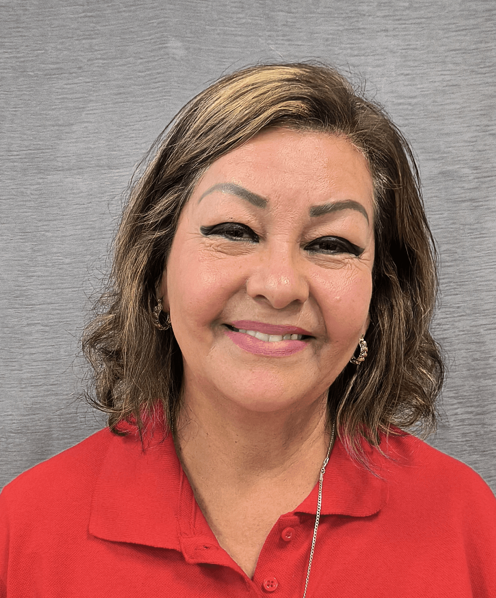 Smiling woman with wavy hair and a red polo shirt against a gray background.