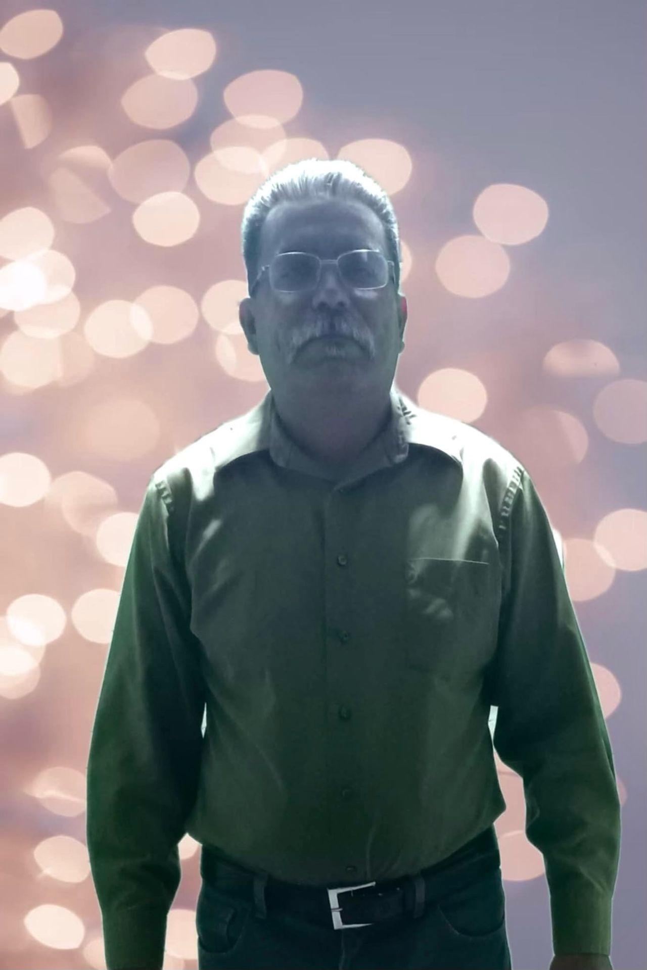 Man in a dark green shirt stands against a background of soft, blurred lights.