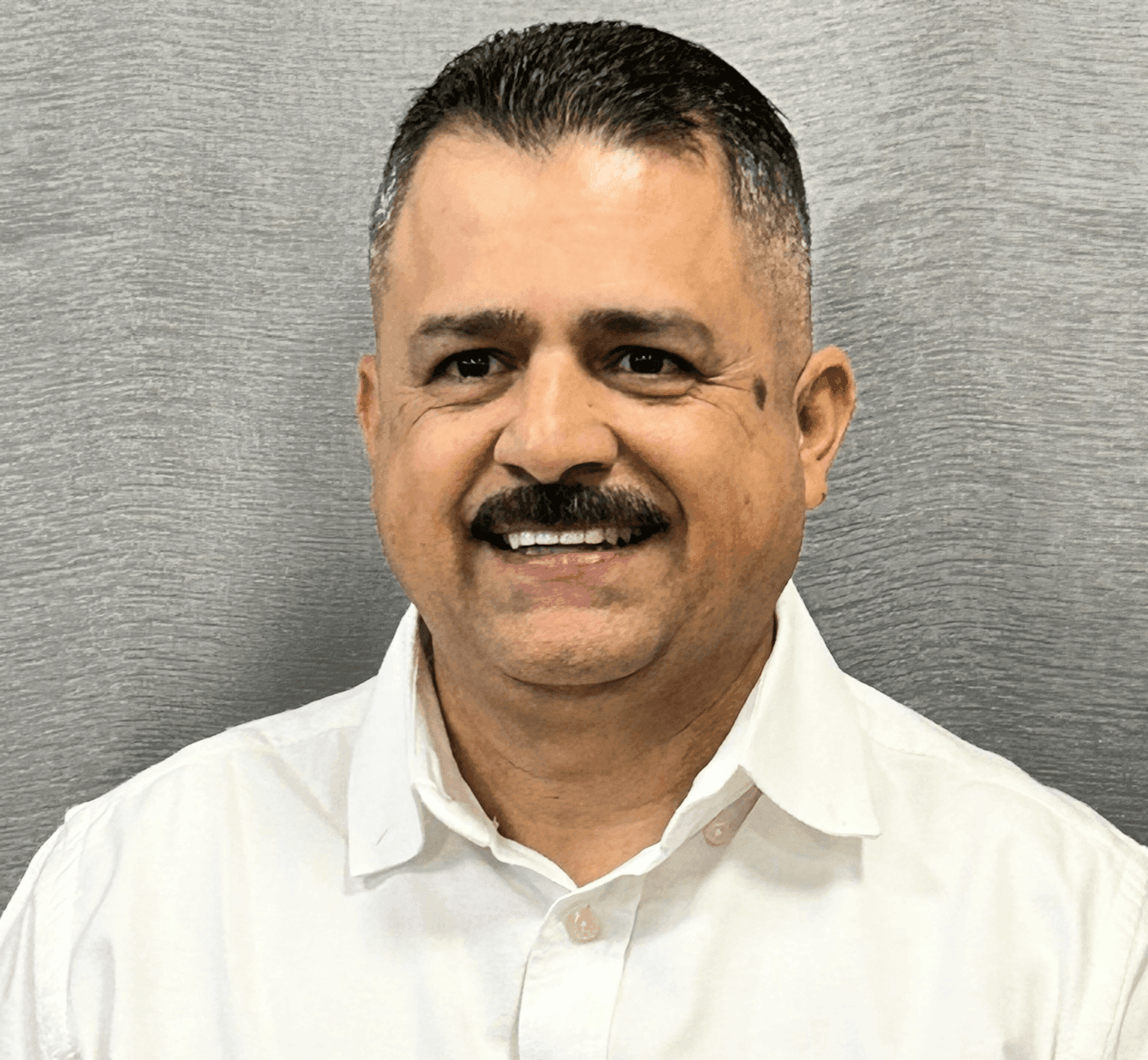 Man with a smile wearing a white shirt in front of a gray background.